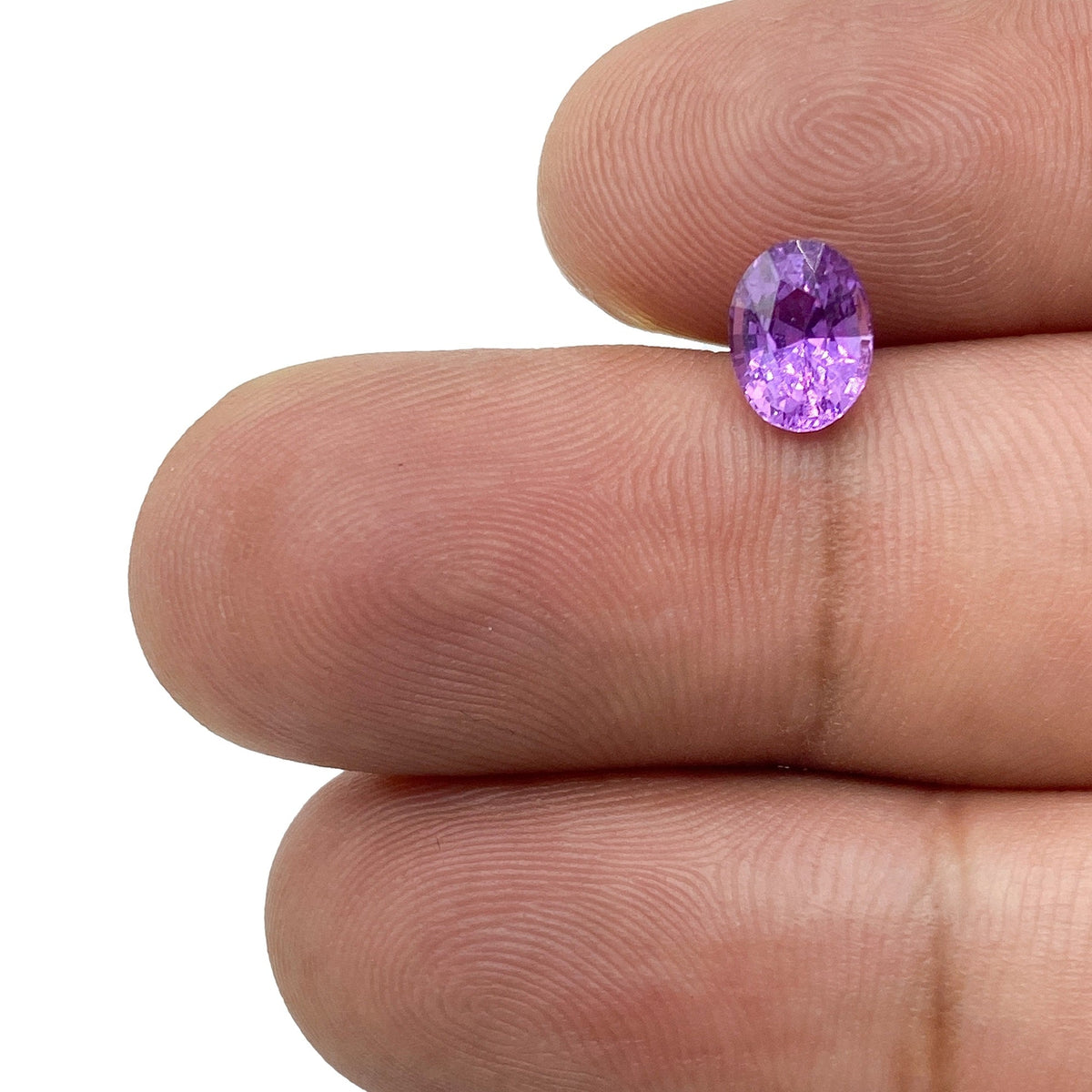 1.14ct oval brilliant cut violet sapphire held between fingers, showcasing its vibrant purple color and faceted surface.