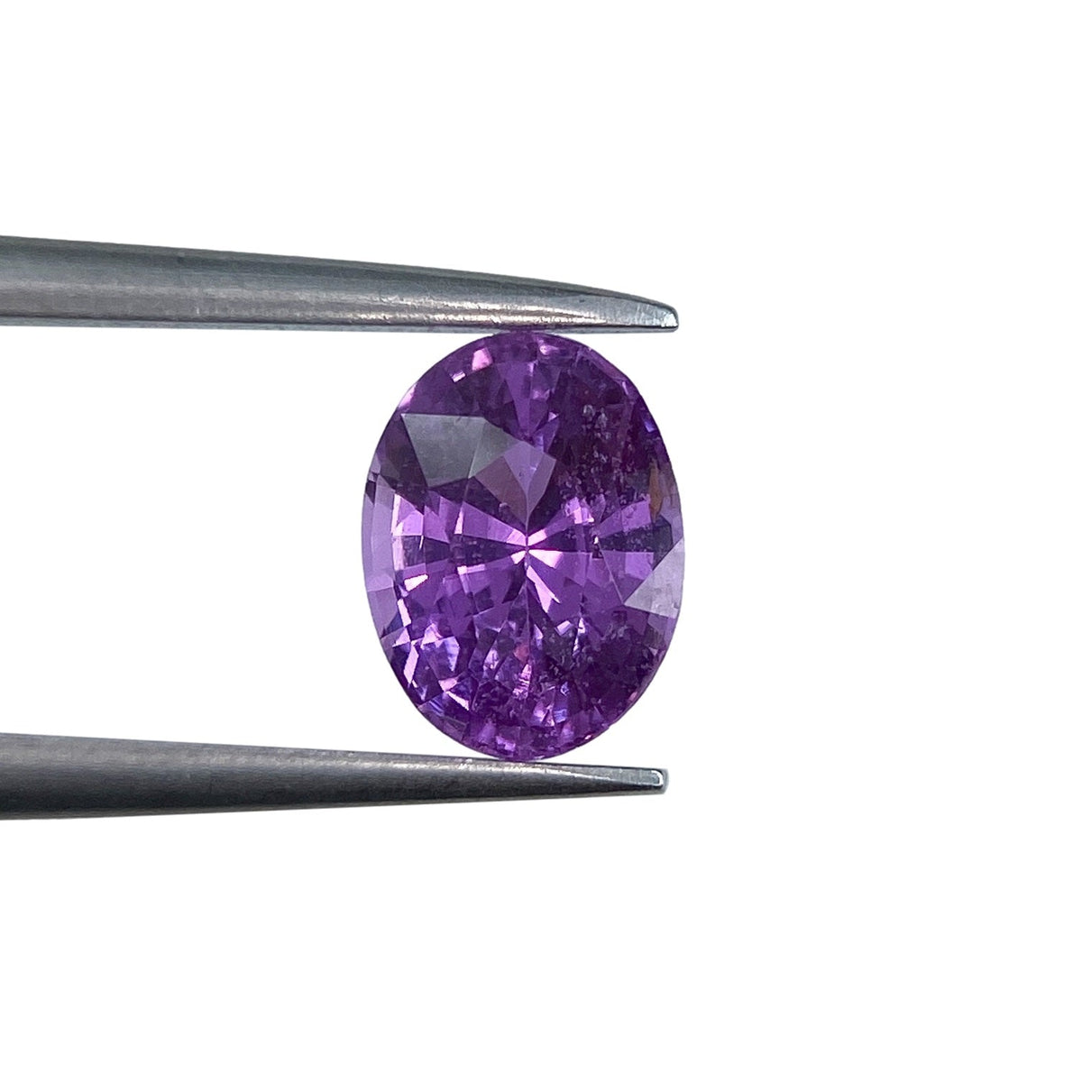 1.14ct oval brilliant cut violet sapphire held in metal tweezers against a white background.