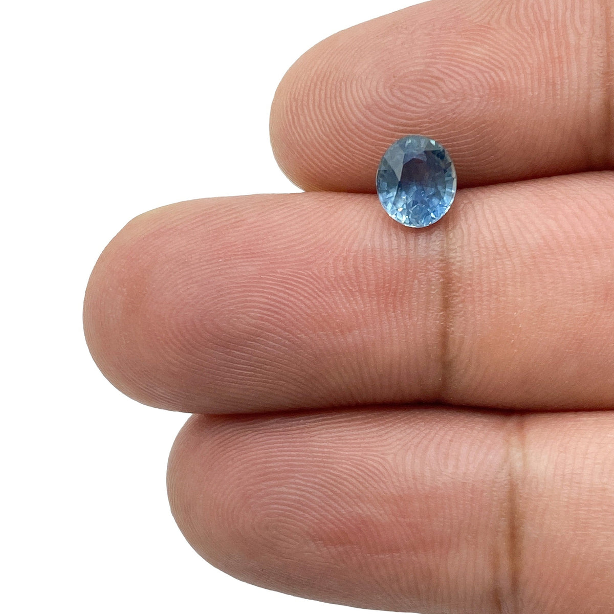 1.15ct oval brilliant cut blue Montana sapphire held between fingers, showing clear facets and vibrant blue color.