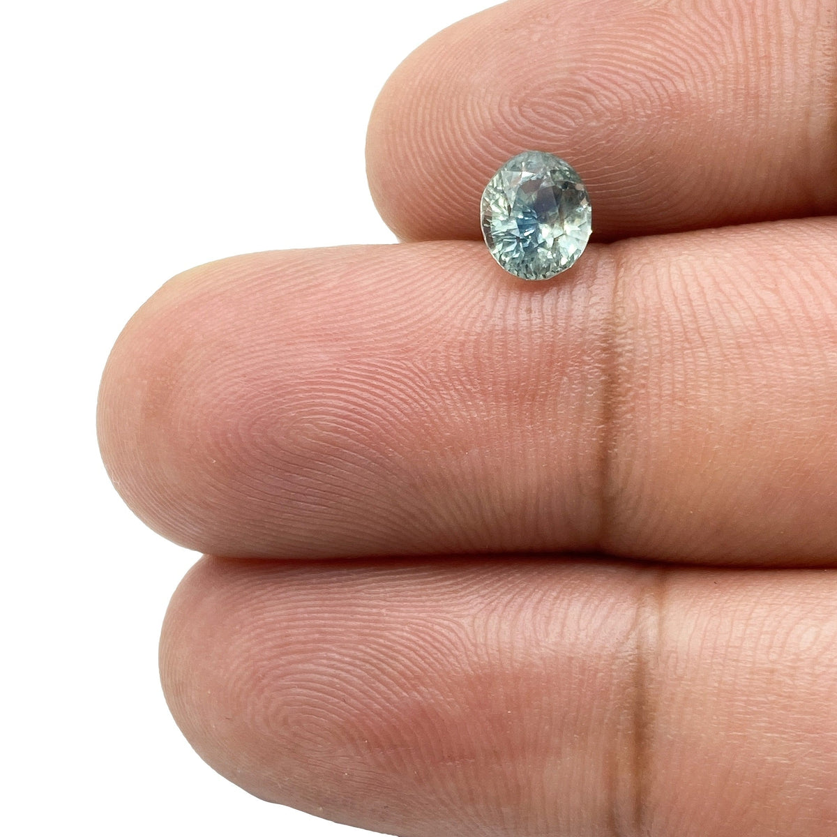1.15ct brilliant cut oval blue Montana sapphire held between fingers.