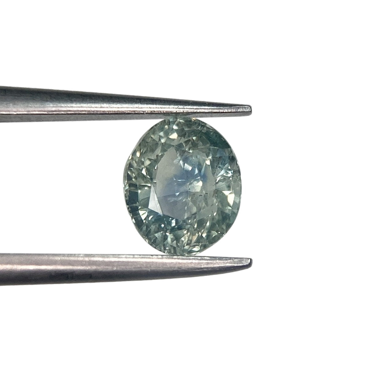 1.15ct brilliant cut oval blue Montana sapphire held in metal tweezers against a white background.