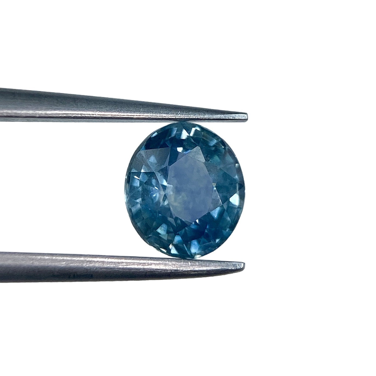 1.15ct brilliant cut oval blue Montana sapphire held in metal tweezers against a white background.