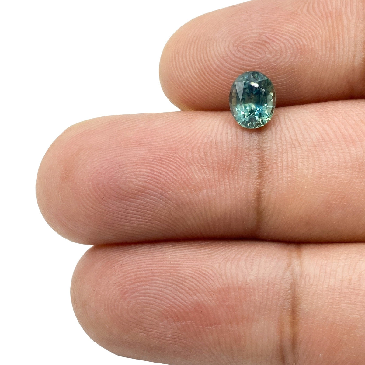 1.15ct oval brilliant cut green Montana sapphire held between fingers, showing natural color and facets.