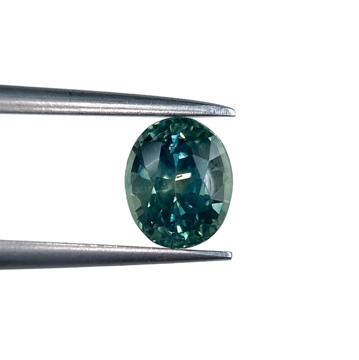 1.15ct oval brilliant cut green Montana sapphire held by metal tweezers against a white background.