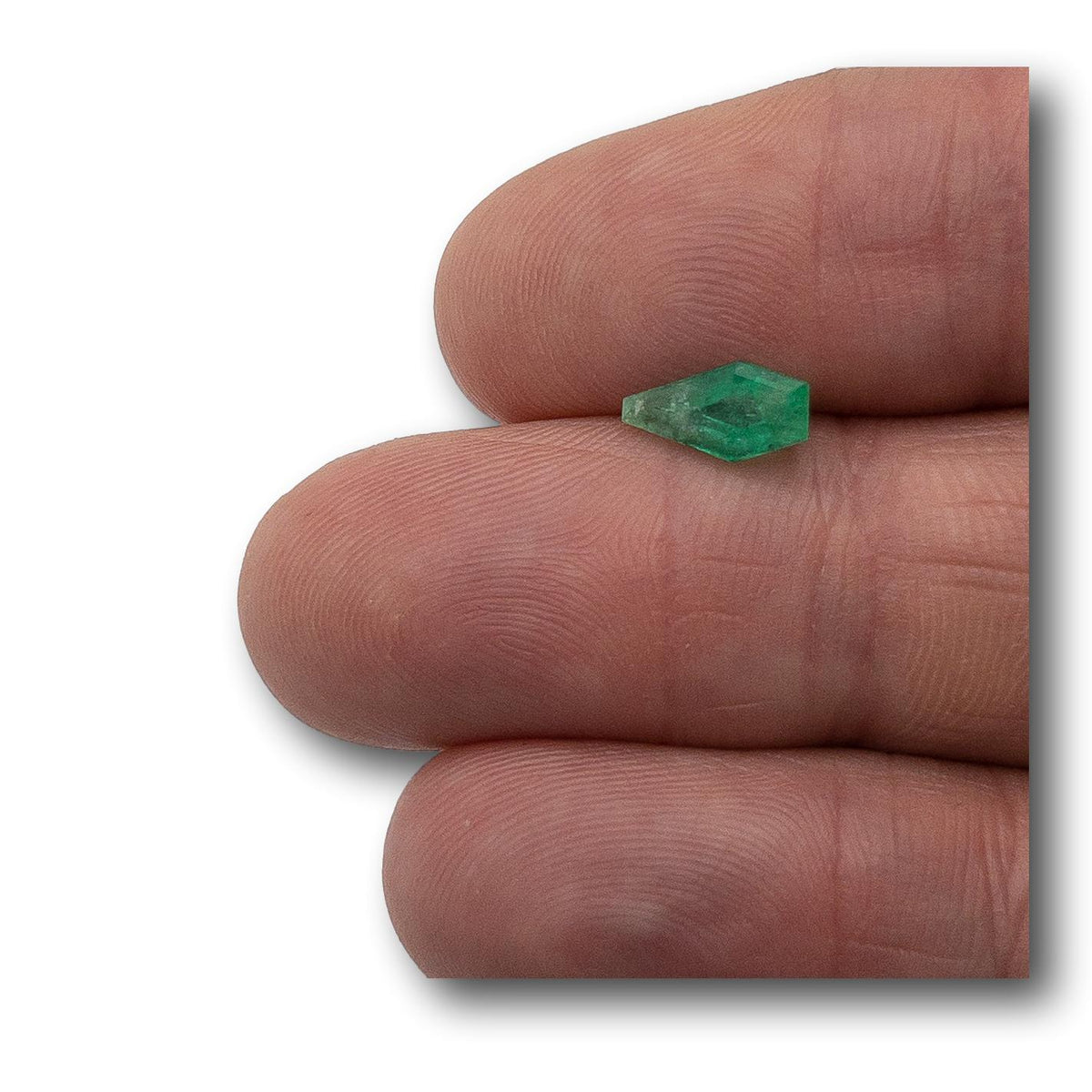 1.15ct step-cut shield-shaped Muzo Colombian emerald held between fingers.