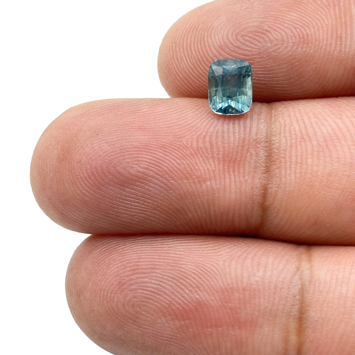 1.16ct cushion-cut blue Montana sapphire with brilliant facets held between fingers.