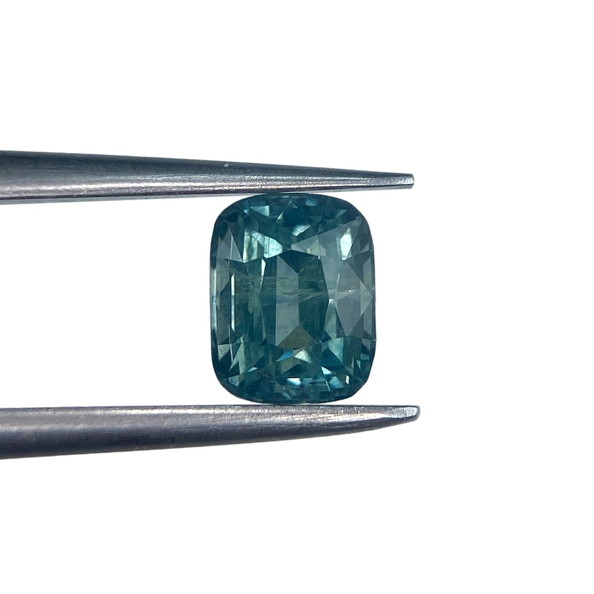 1.16ct brilliant cut cushion-shaped blue Montana sapphire held in metal tweezers against a white background.