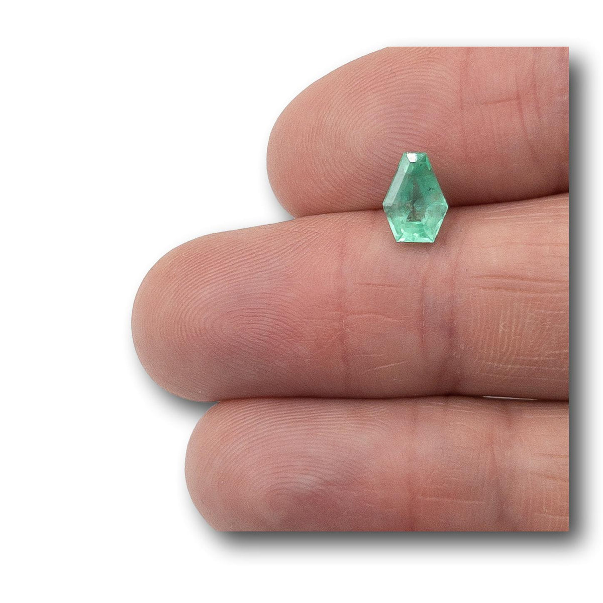 1.16ct shield-cut Muzo emerald with a vibrant green hue held between fingers.