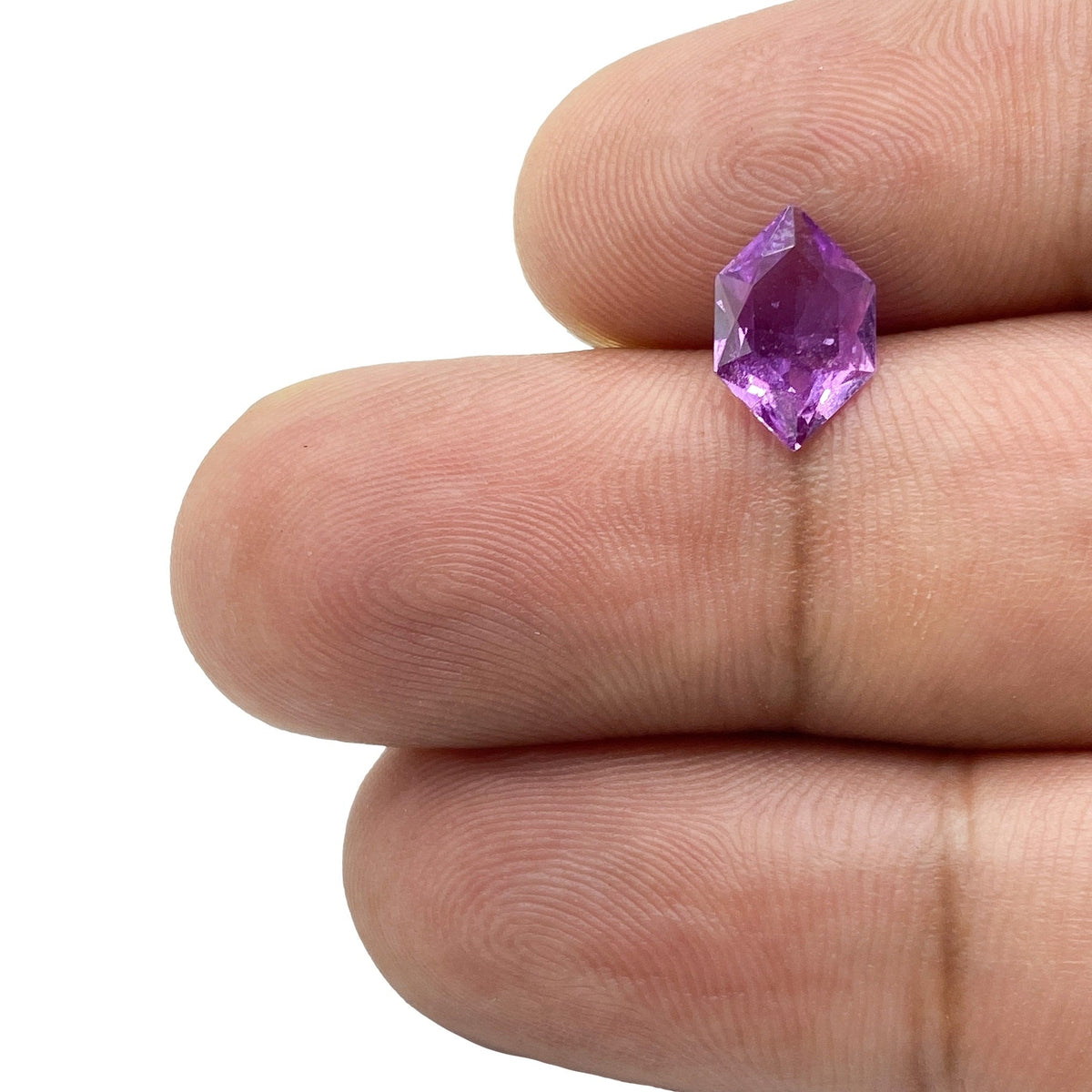 1.17ct brilliant cut violet sapphire in a unique hexagon shape held between fingers against a white background.