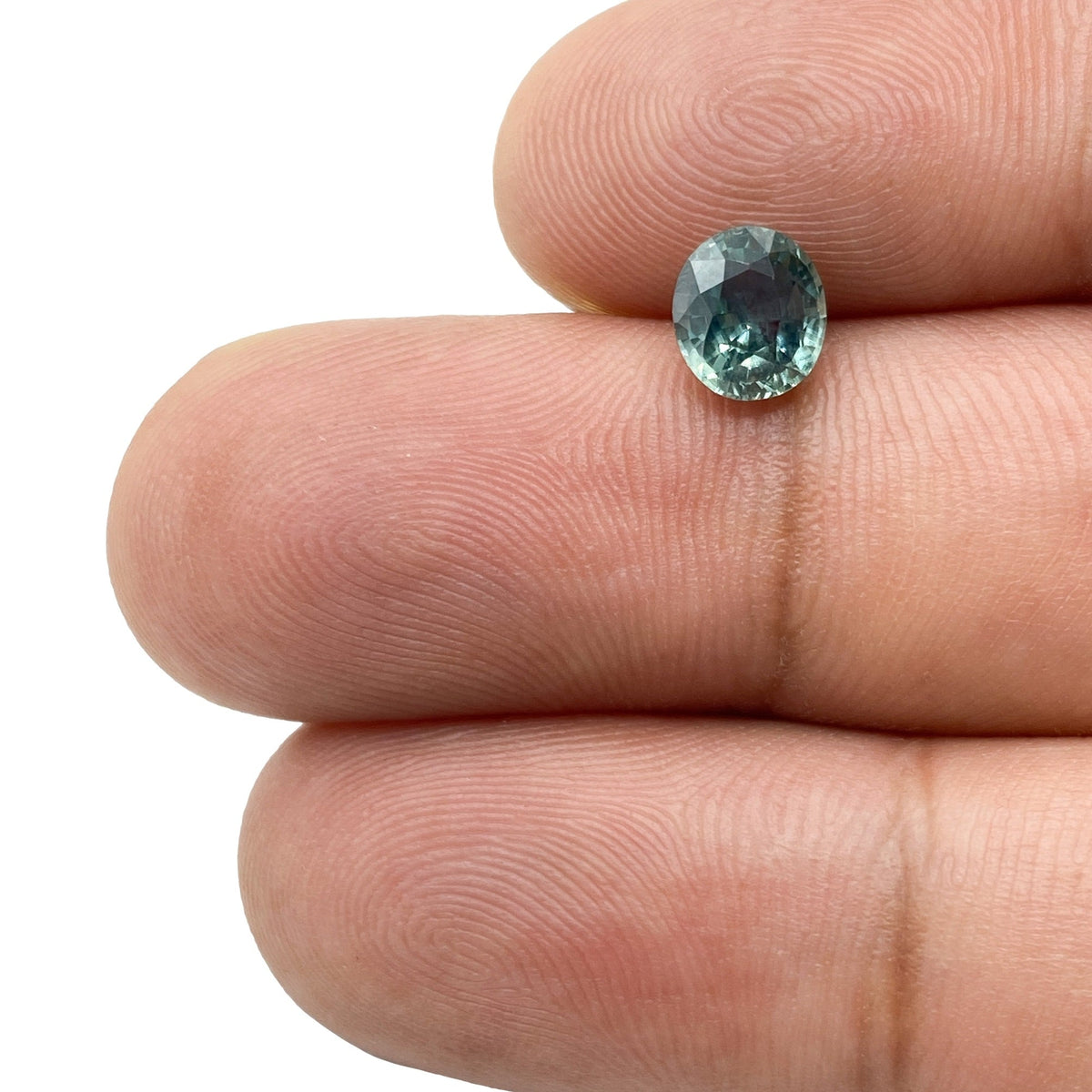 1.17ct oval brilliant cut blue Montana sapphire gemstone held between fingers.