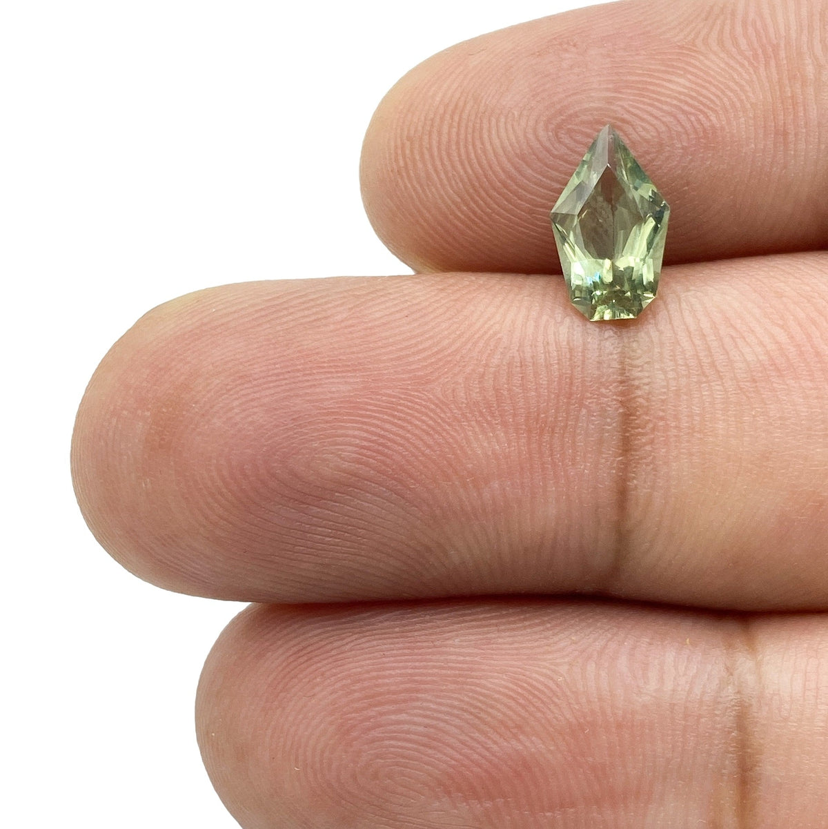 1.17ct brilliant cut green sapphire in a unique shield shape held between fingers.
