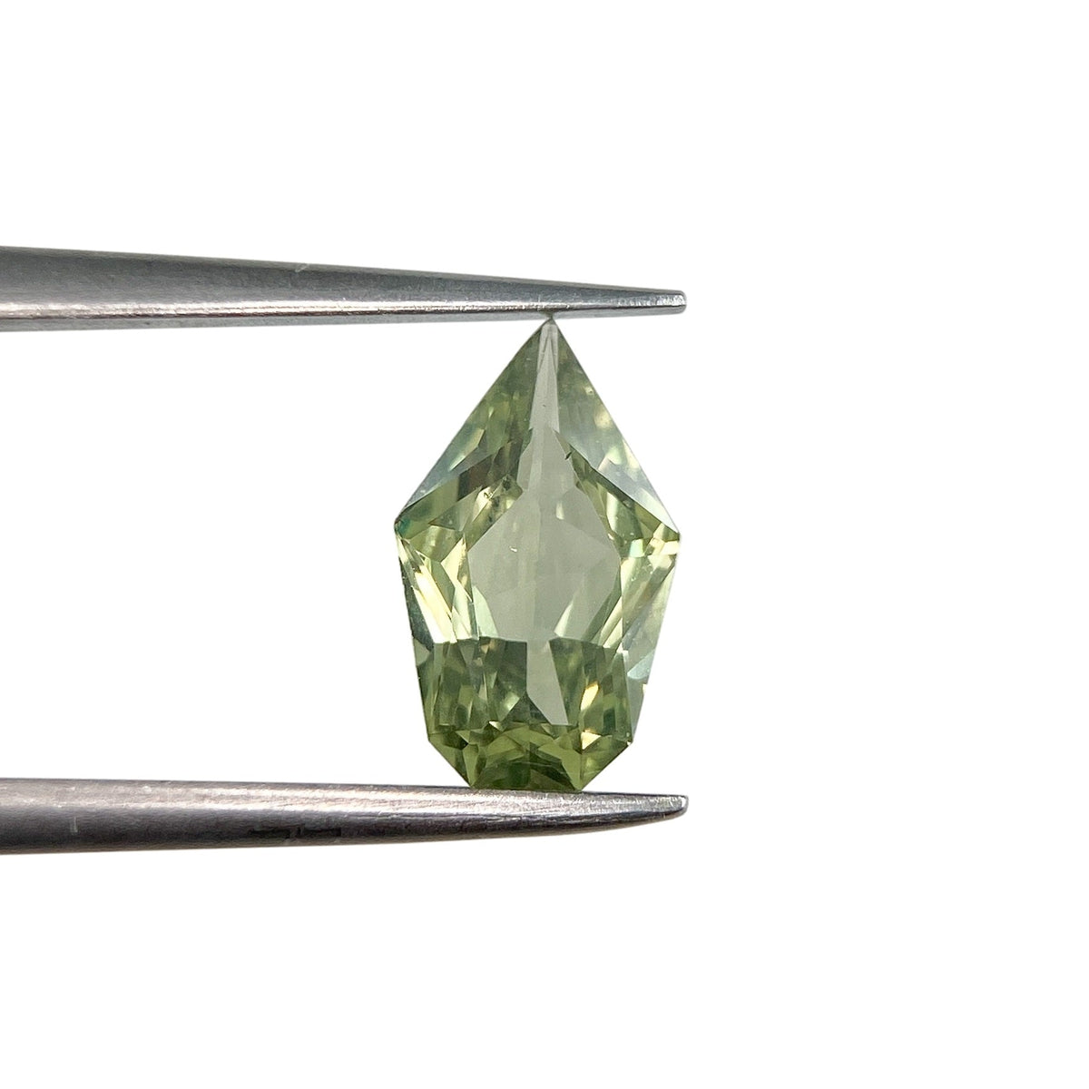 1.17ct brilliant cut green sapphire in a unique shield shape held by metal tweezers against a white background.