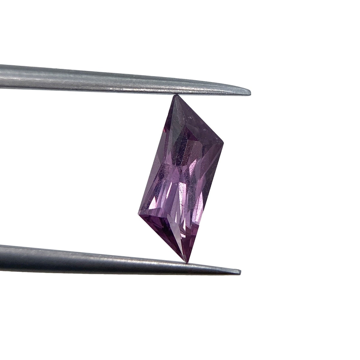 1.18ct brilliant cut violet sapphire in a unique rhomboid shape held by metal tweezers against a white background.