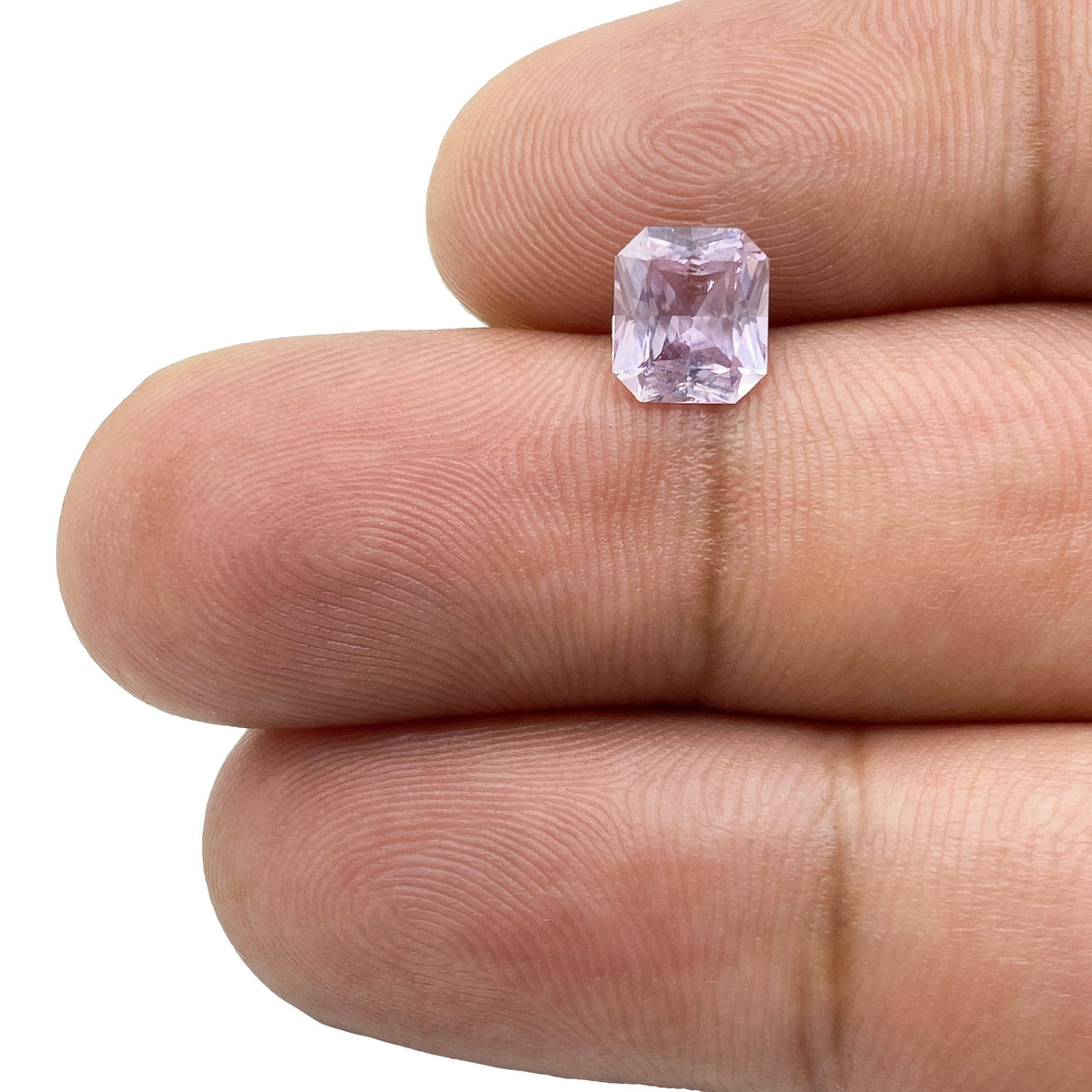 1.25ct radiant cut pink sapphire gemstone held between fingers, showcasing its soft pink hue and faceted rectangular shape.
