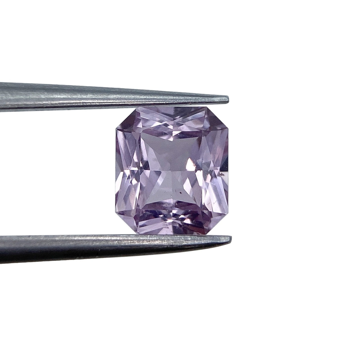 1.25ct radiant cut pink sapphire gemstone held in metal tweezers against a white background.