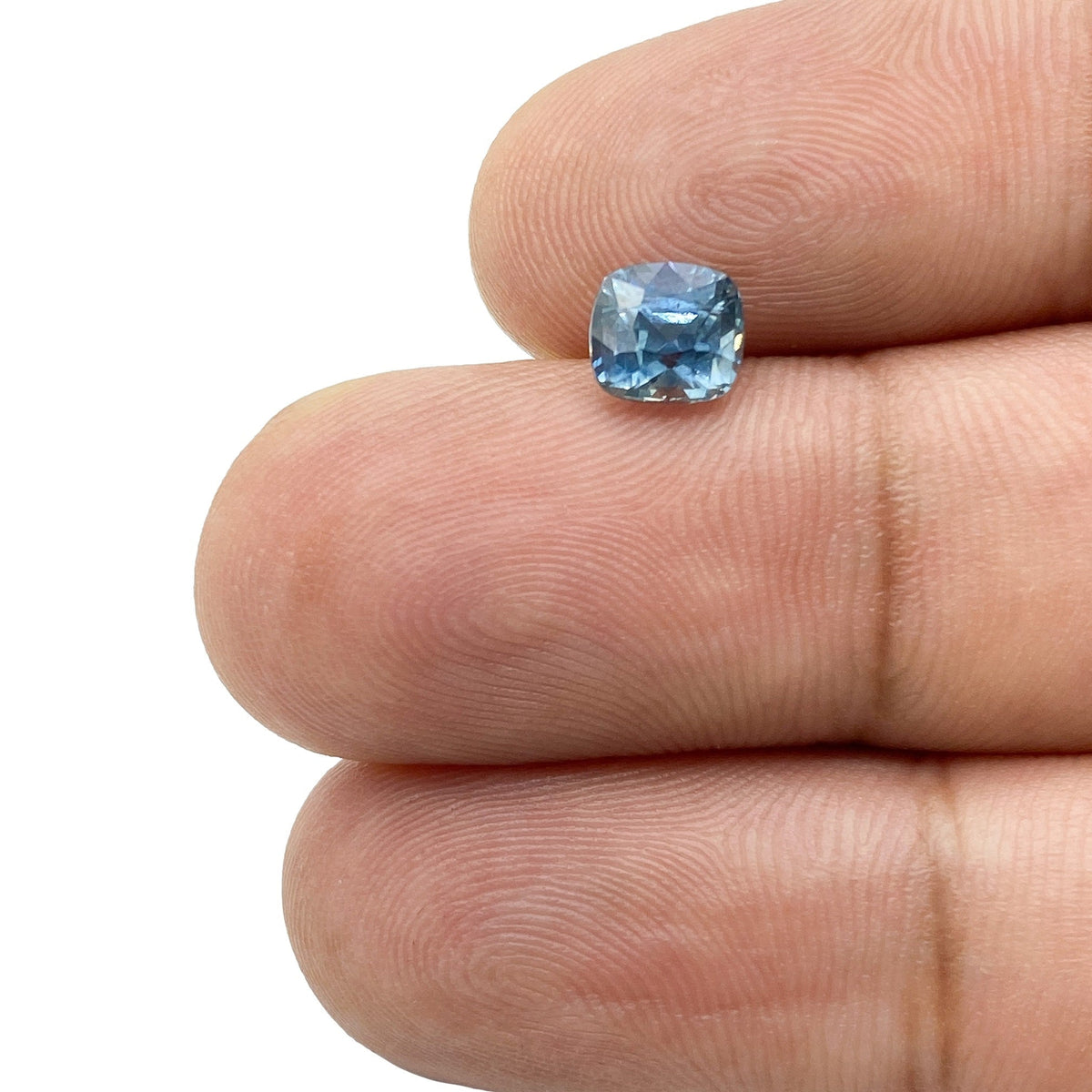1.26ct brilliant cut cushion shape blue Montana sapphire held between fingers.