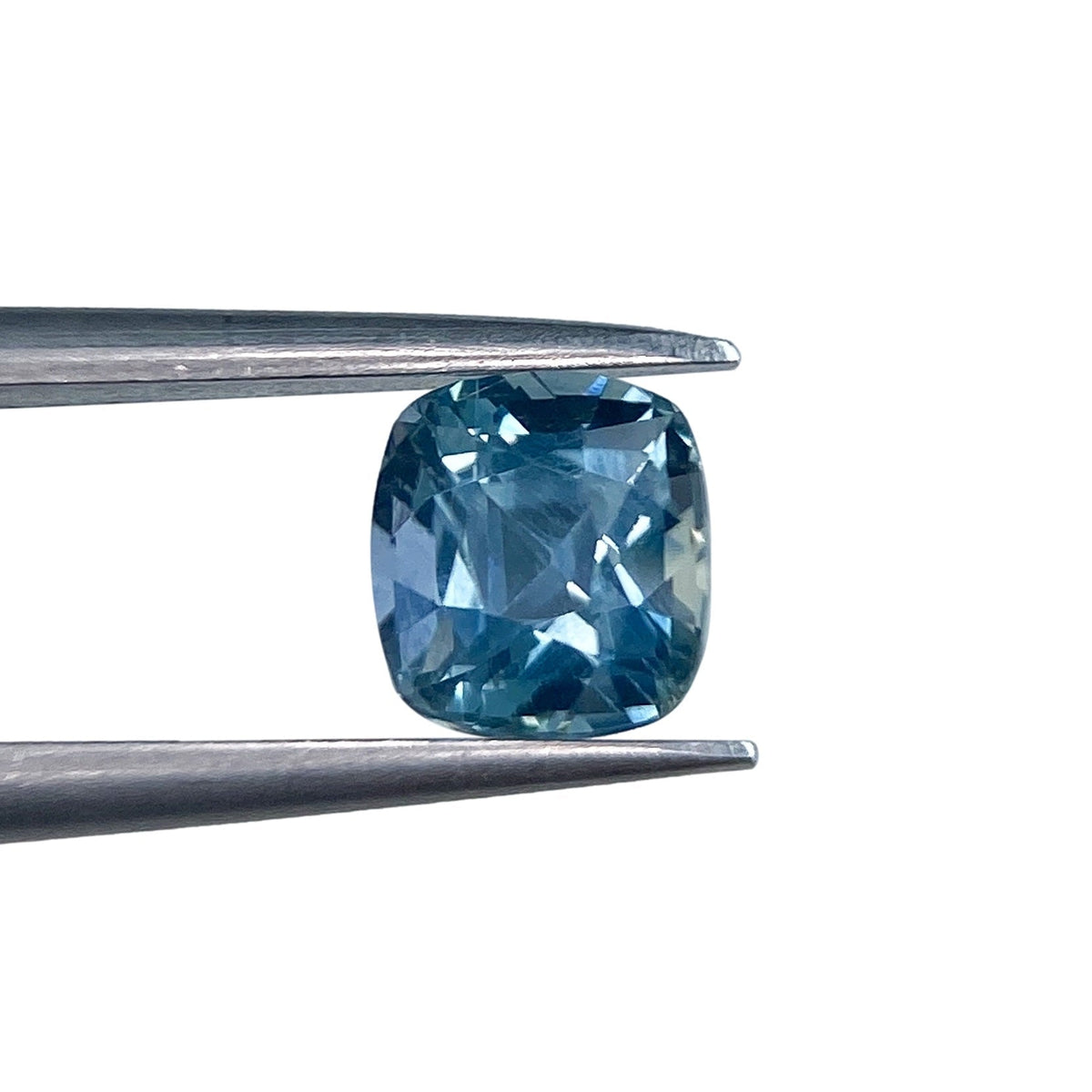 1.26ct brilliant cut cushion-shaped blue Montana sapphire held in metal tweezers against a white background.