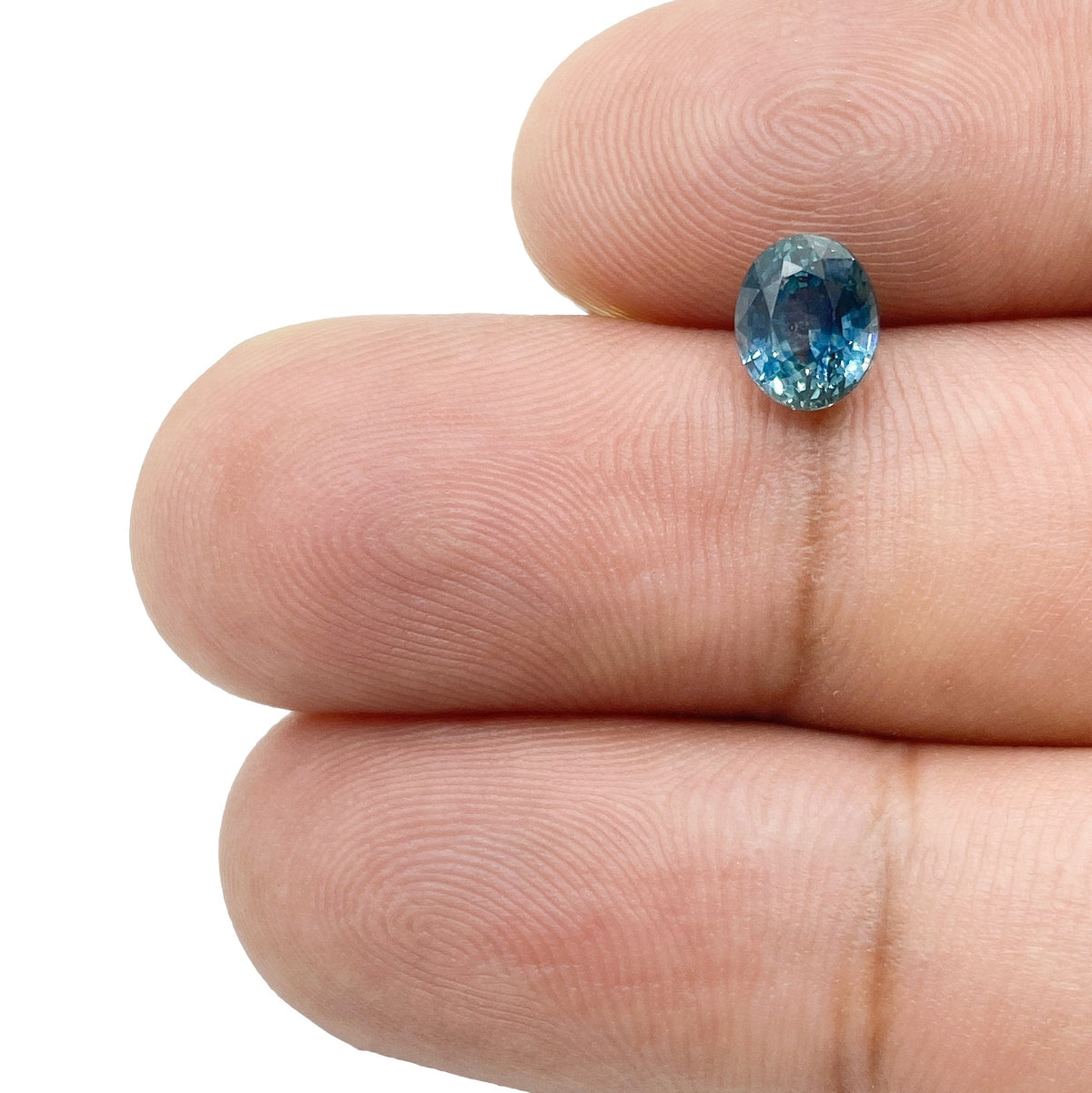 1.27ct oval brilliant cut blue Montana sapphire held between fingers, showing its faceted sparkle and deep blue color.