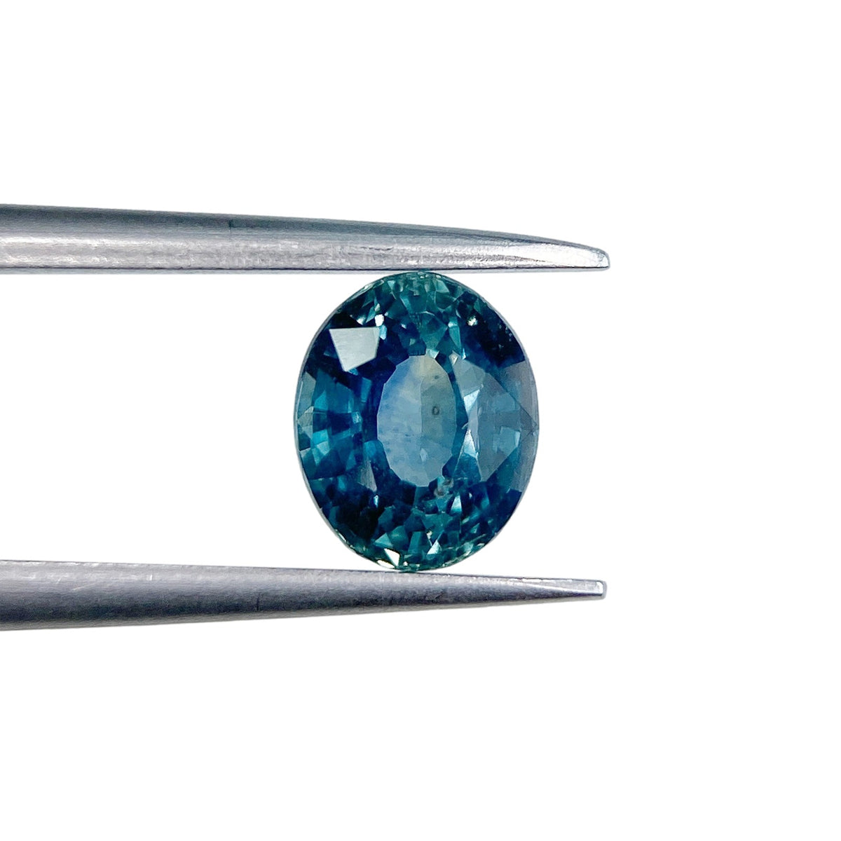 1.27ct oval brilliant cut blue Montana sapphire held in metal tweezers against a white background.