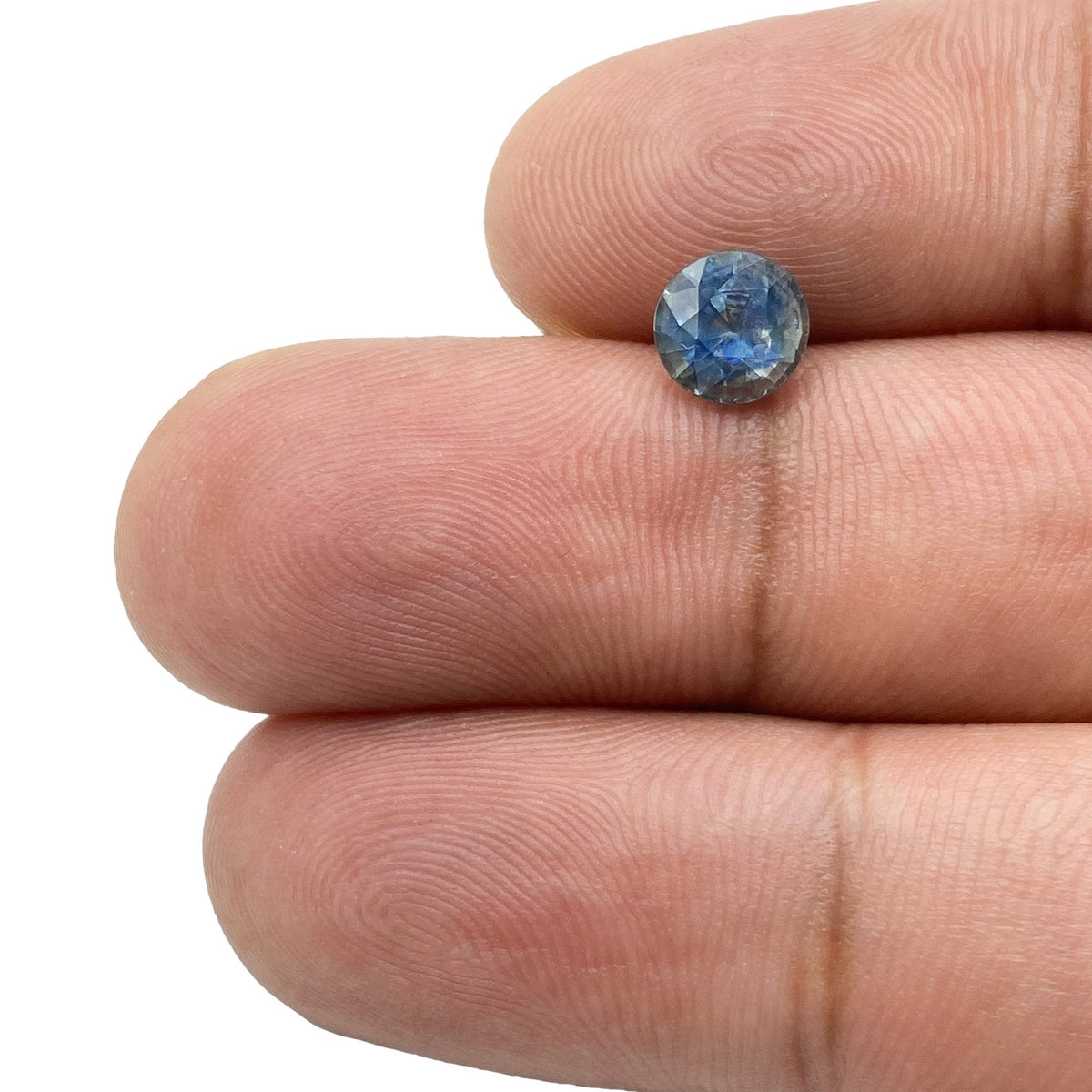 1.28ct round brilliant cut blue Montana sapphire held between two fingers.