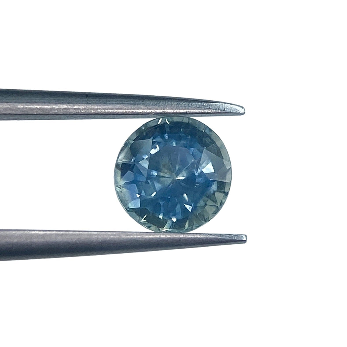 1.28ct round brilliant cut blue Montana sapphire held in metal tweezers against a white background.