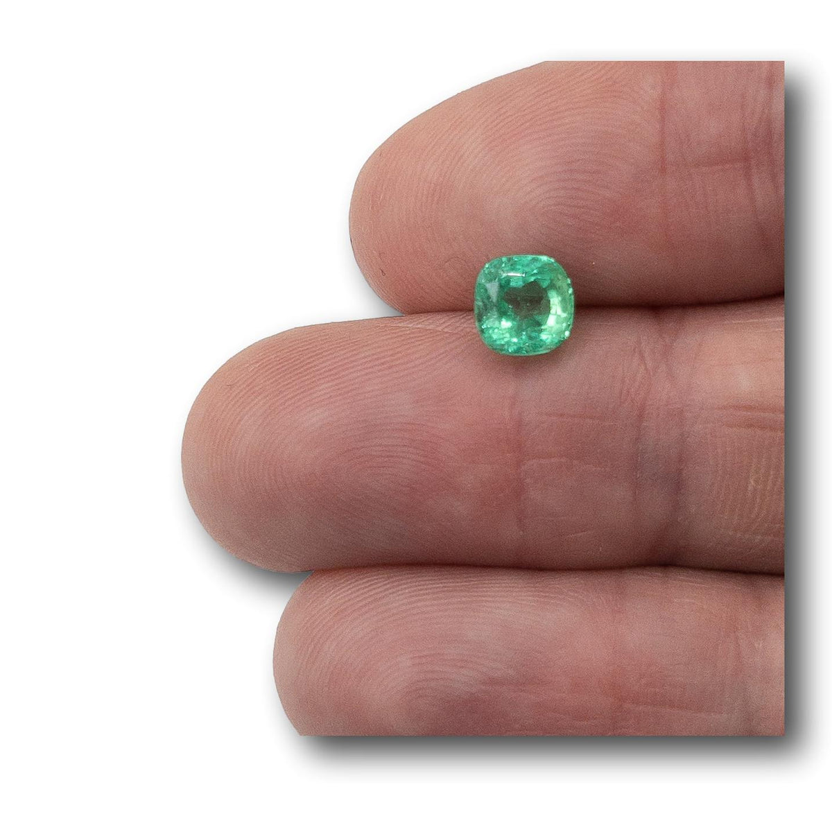 1.29ct brilliant cut cushion-shaped Muzo emerald held between fingers, showcasing a vibrant green gemstone.