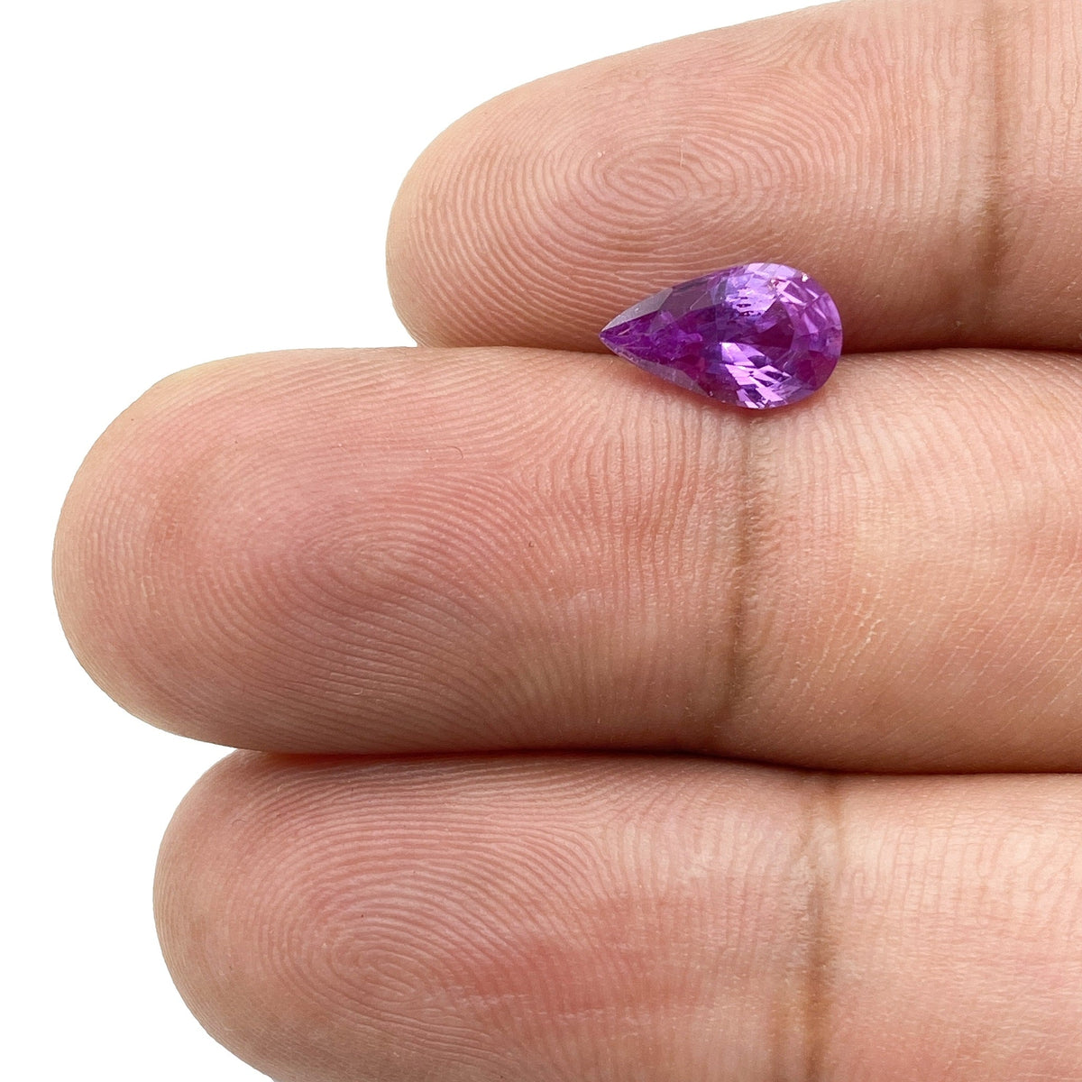 1.32ct brilliant cut pear-shaped violet sapphire gemstone held on a finger against a white background.