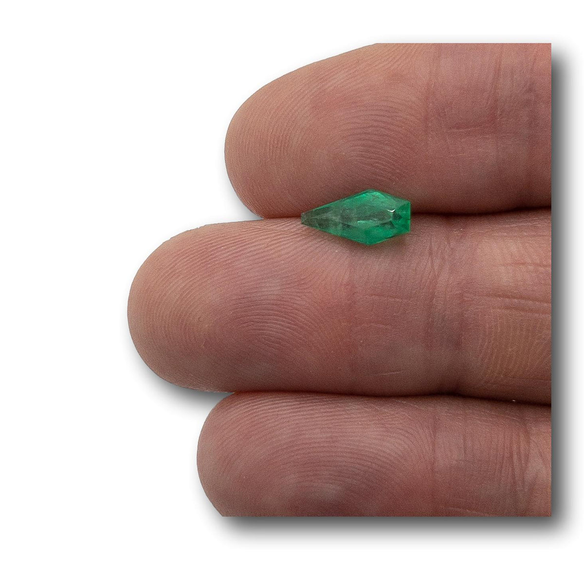 1.33ct step cut shield-shaped Muzo emerald held between fingers, showcasing a vibrant green gemstone.