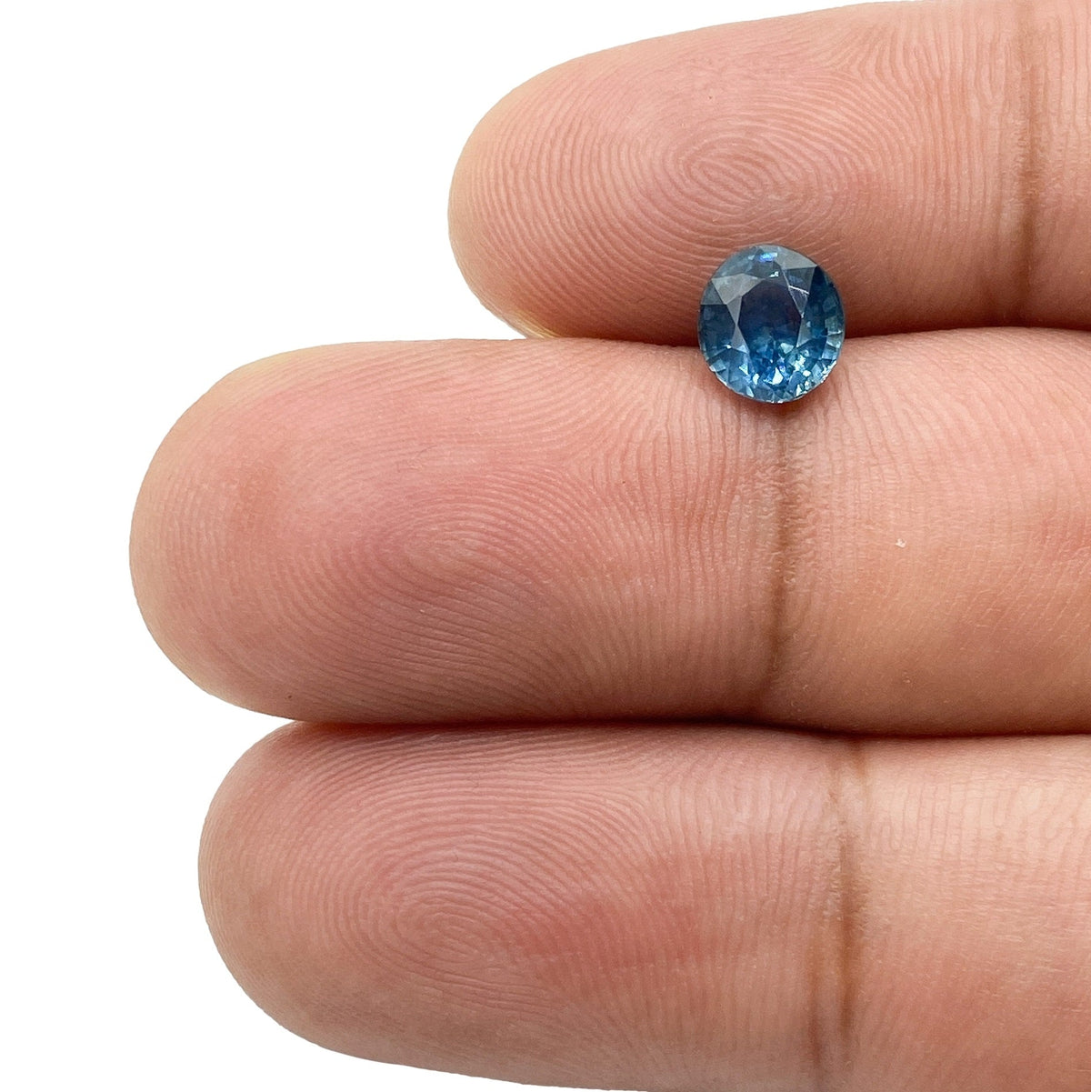 1.40ct brilliant cut oval blue Montana sapphire held between fingers, showcasing its faceted sparkle and deep blue hue.