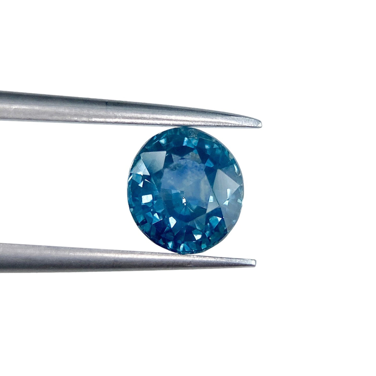 1.40ct brilliant cut oval blue Montana sapphire held in metal tweezers against a white background.
