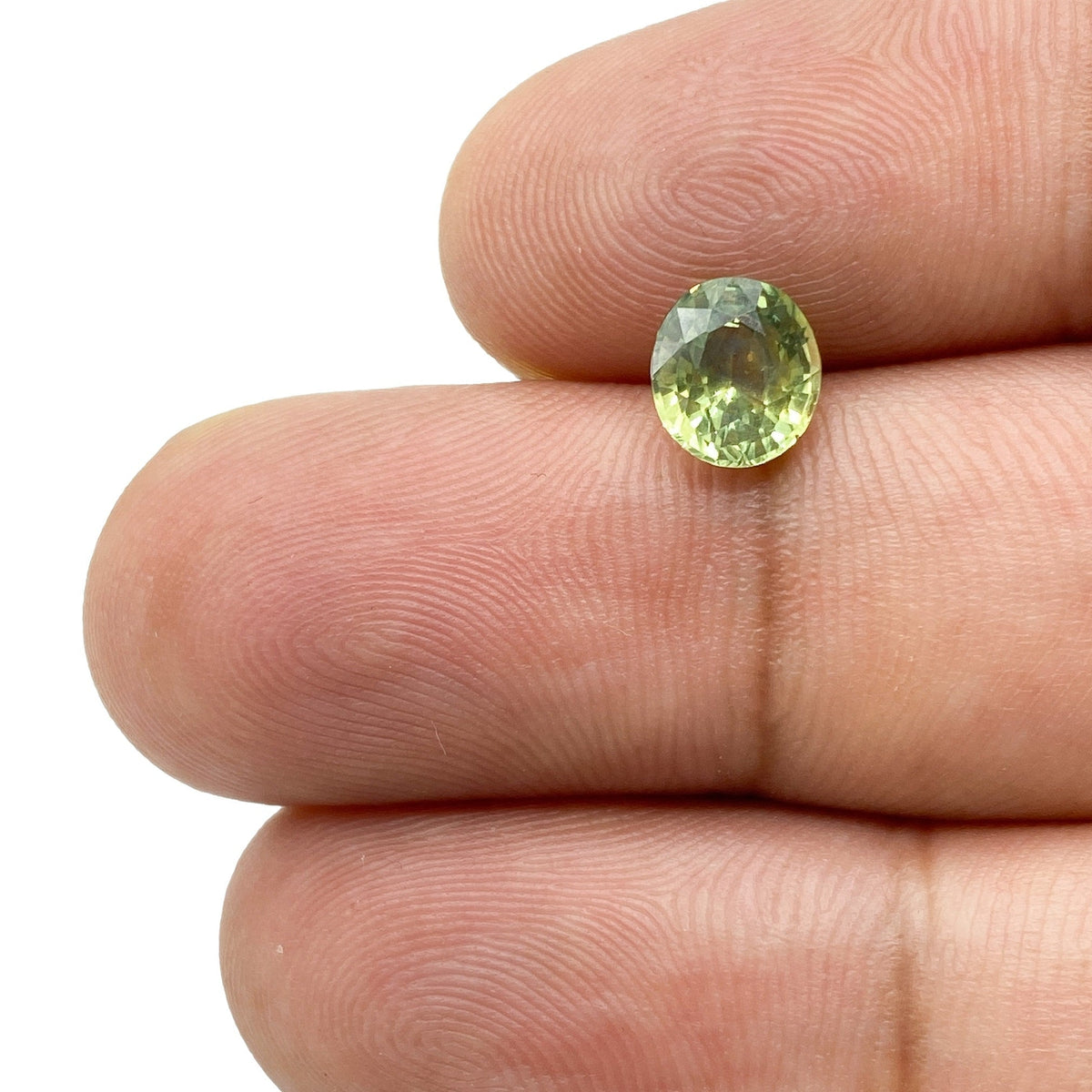 1.41ct oval brilliant cut green Montana sapphire held between fingers, showing natural color and faceted clarity.