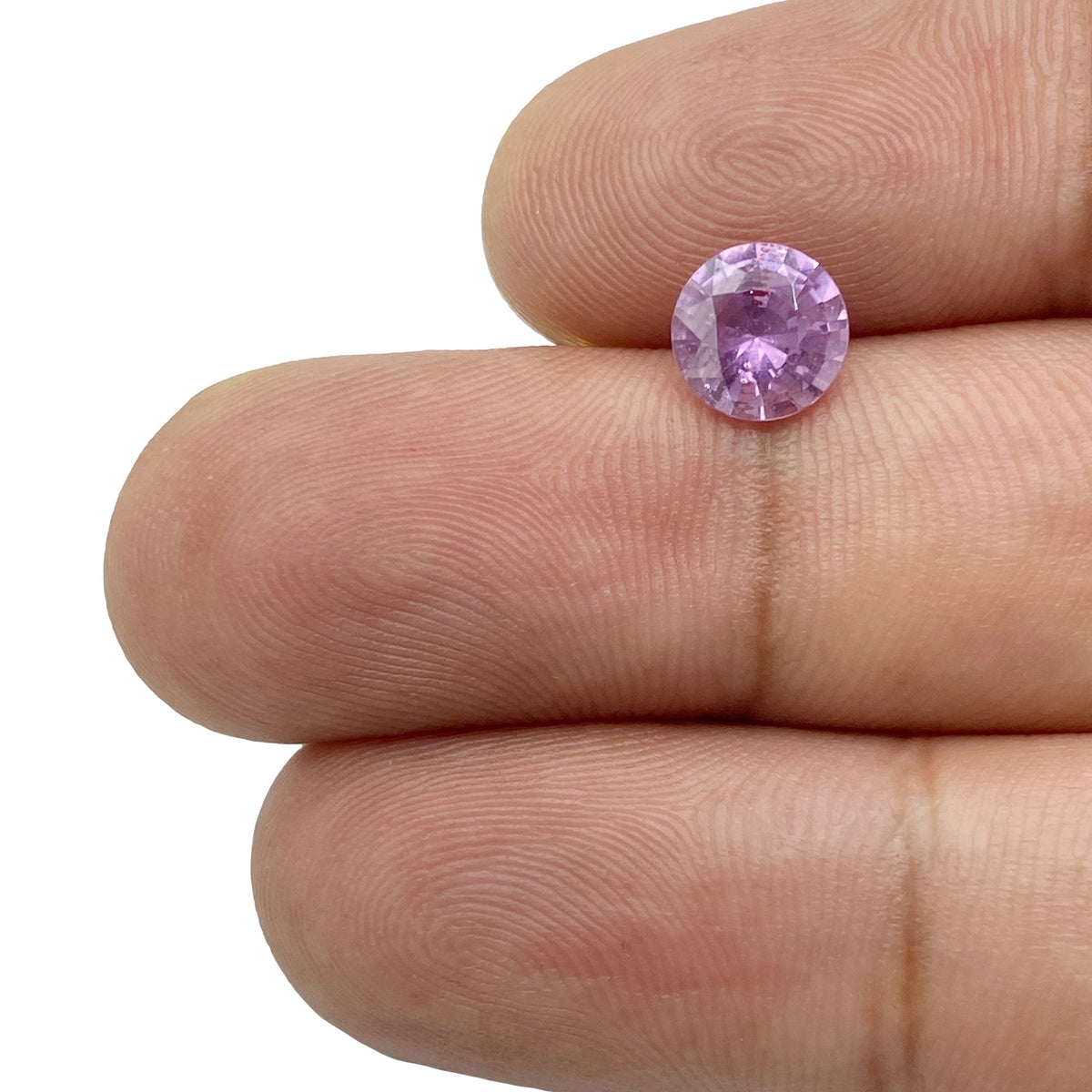 1.44ct round brilliant cut violet sapphire held between fingers, showcasing its vibrant color and faceted design.