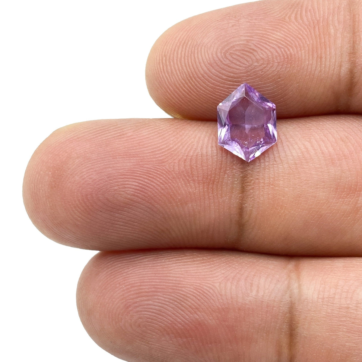 1.45ct brilliant cut violet sapphire with a unique hexagon shape held between fingers.