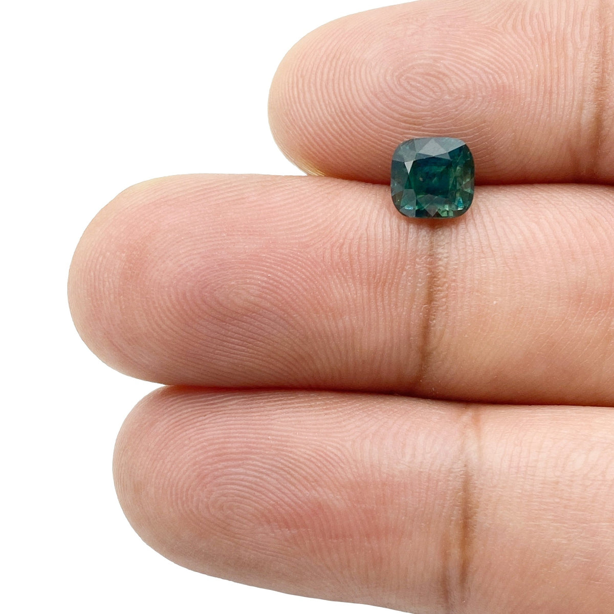 1.46ct brilliant cut cushion-shaped green Montana sapphire held between fingers.