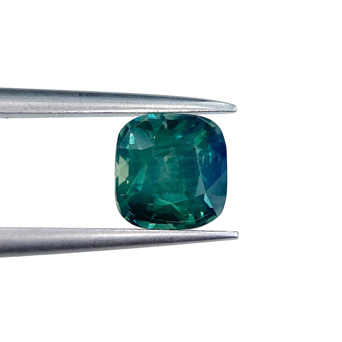 1.46ct brilliant cut cushion-shaped green Montana sapphire held in metal tweezers against a white background.