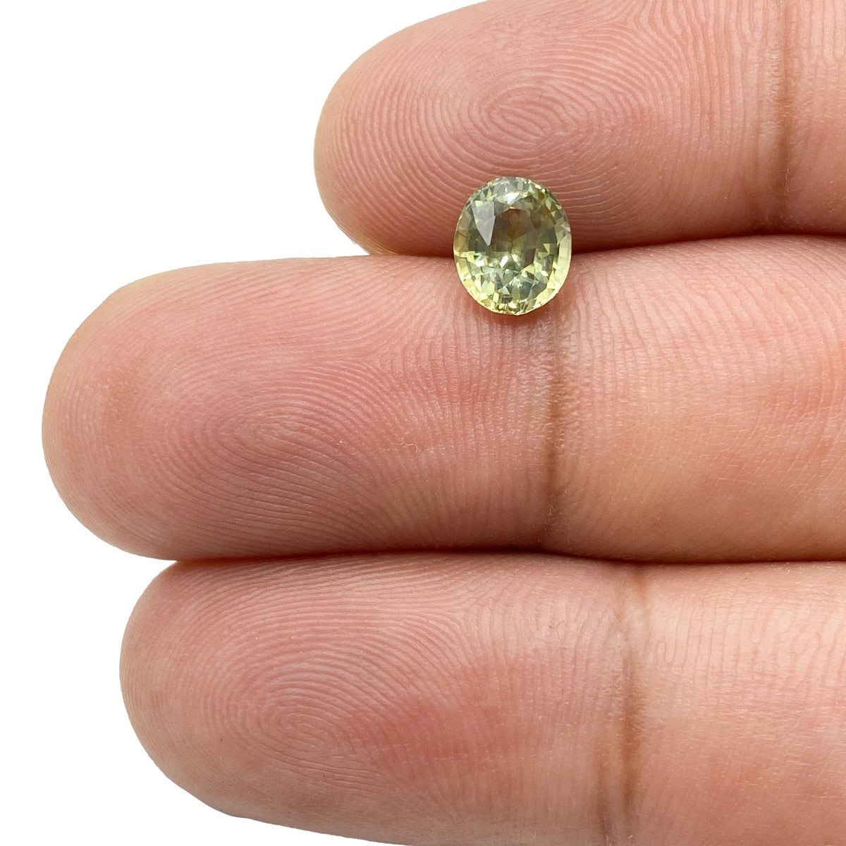 1.48ct oval brilliant cut green Montana sapphire held between fingers, showcasing its faceted sparkle.