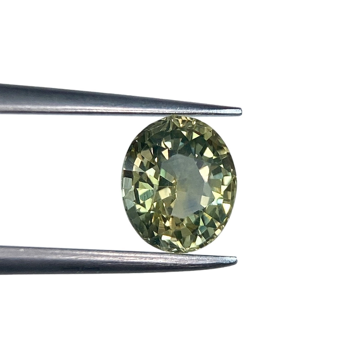 1.48ct oval brilliant cut green Montana sapphire held in metal tweezers against a white background.