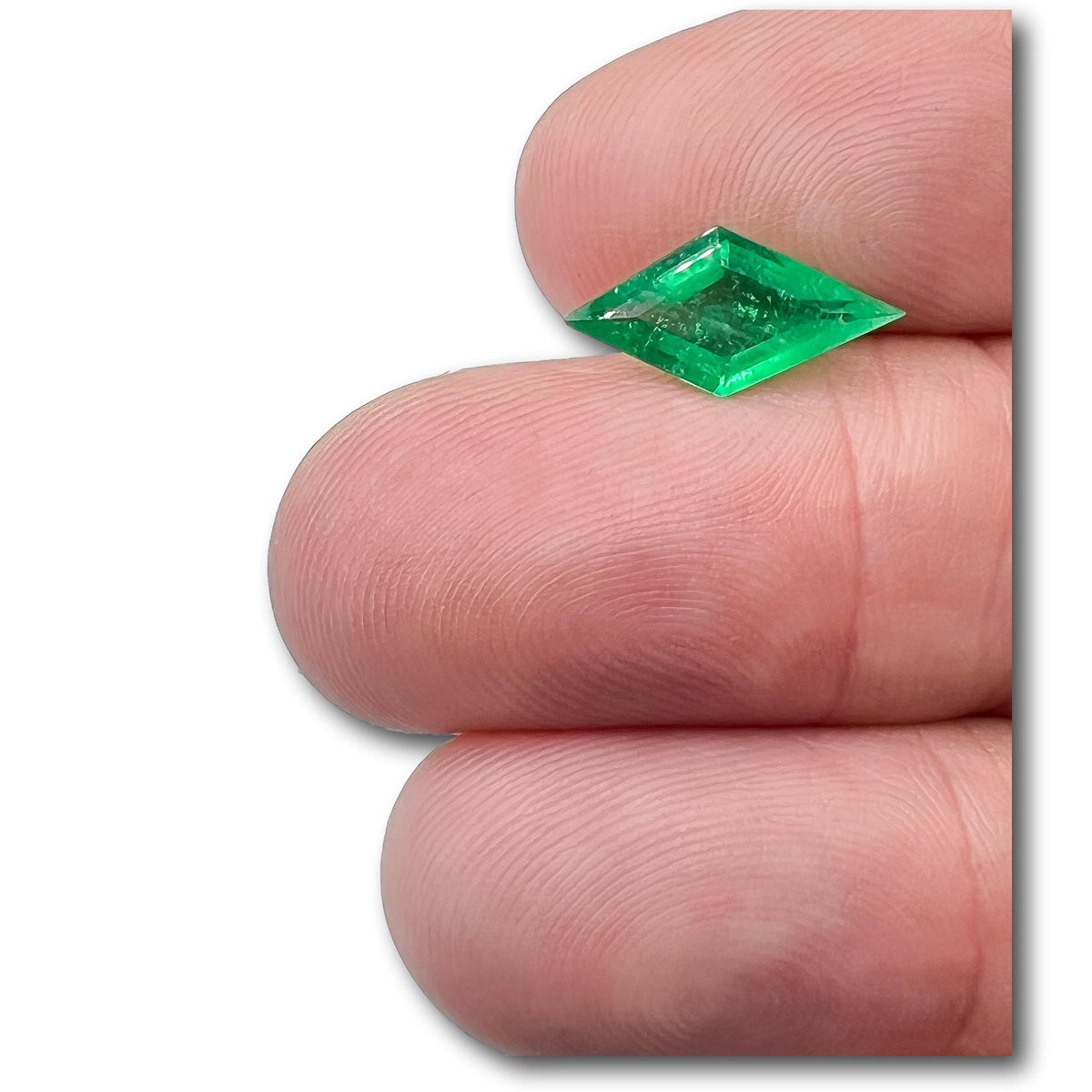 1.49ct Muzo emerald with a unique lozenge step cut, held between fingers to show its vibrant green color and elongated shape.