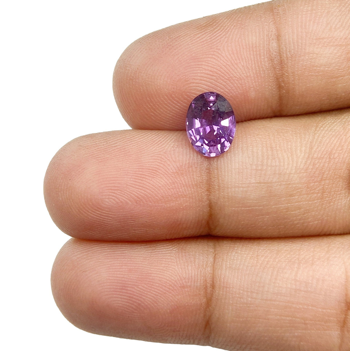 1.58ct oval brilliant cut violet sapphire gemstone held between fingers, showcasing vibrant purple facets and clarity.