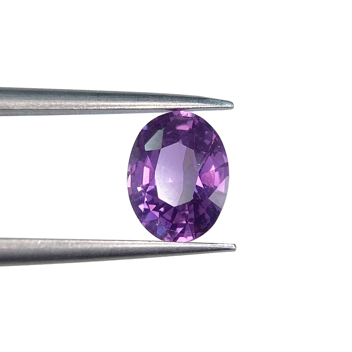 1.58ct oval brilliant cut violet sapphire held in metal tweezers against a white background.