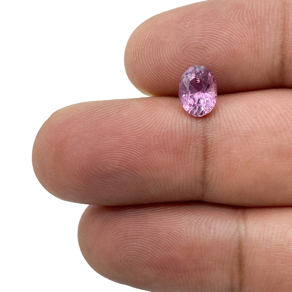 1.59ct brilliant cut oval violet sapphire held between fingers, showcasing its faceted gemstone clarity and vibrant color.