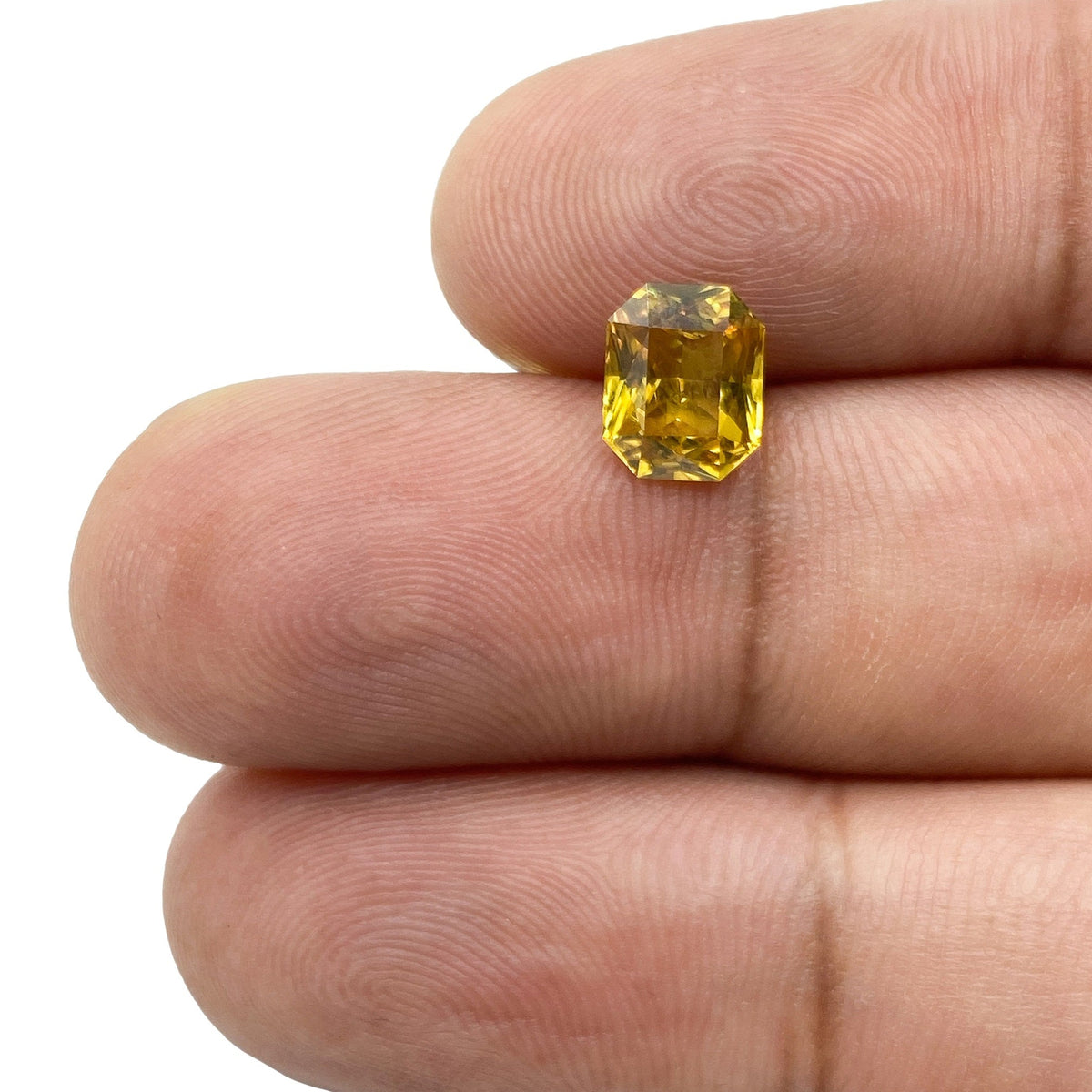 1.62ct radiant cut yellow sapphire gemstone held between fingers, showcasing a vibrant golden hue and precise facets.