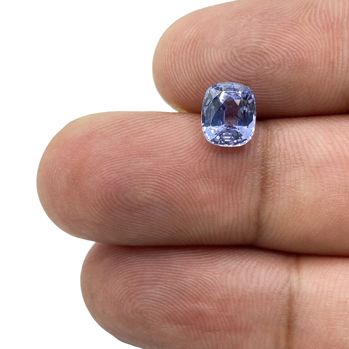 1.64ct brilliant cut cushion-shaped blue spinel gemstone held between fingers.