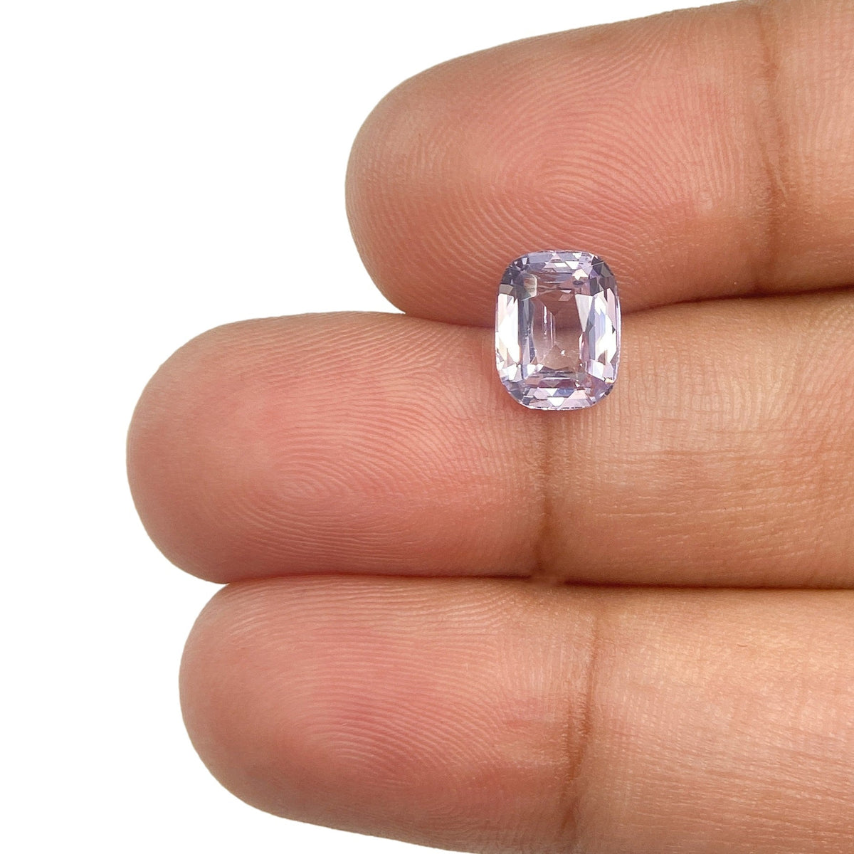 1.71ct cushion-cut blue spinel gemstone with a brilliant facet pattern held between fingers.