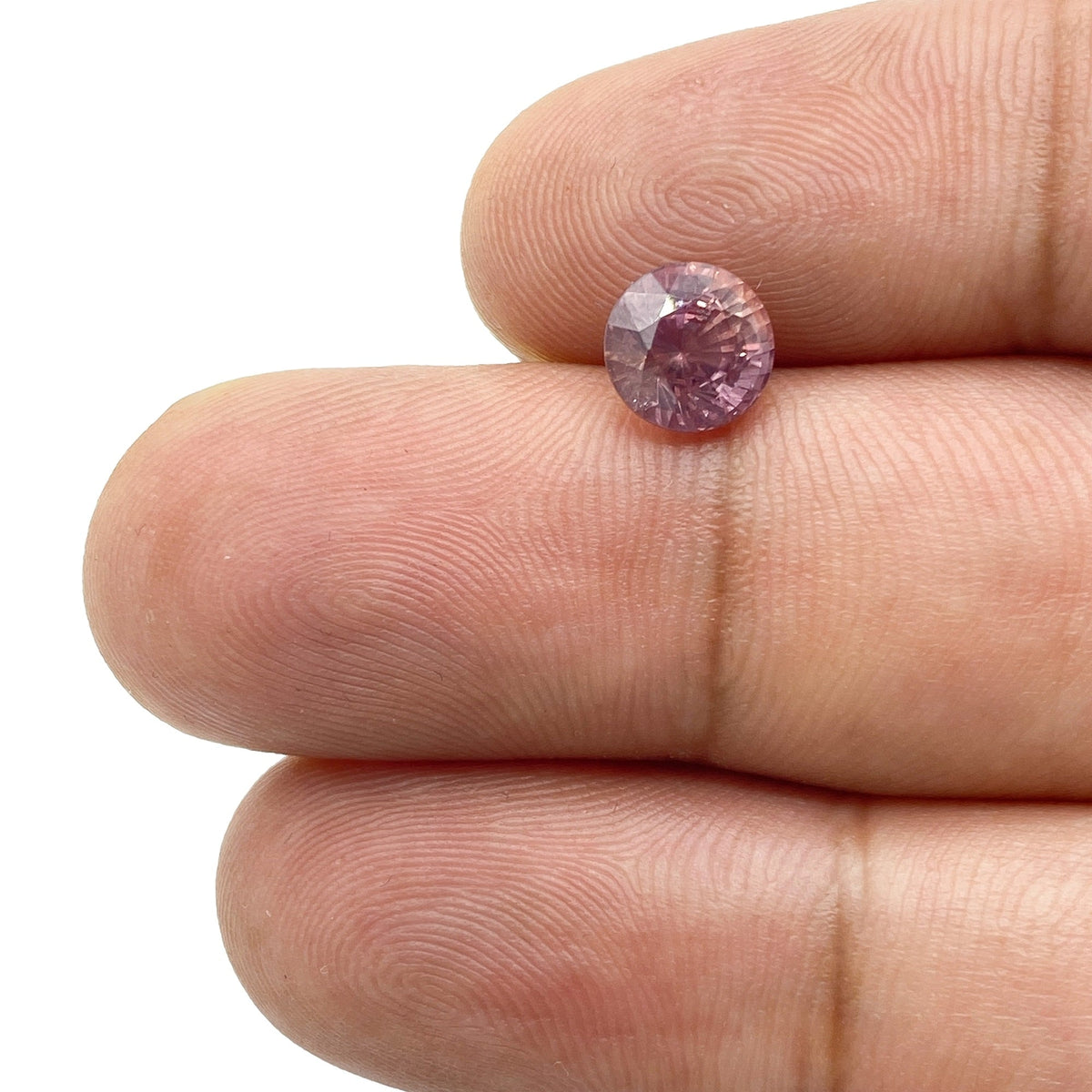 1.72ct round brilliant cut pink sapphire held between fingers, showcasing its vibrant color and faceted gemstone surface.