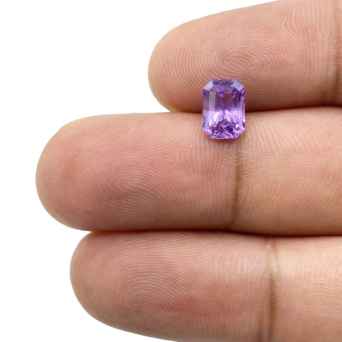 1.77ct radiant cut violet sapphire gemstone held between fingers, showcasing a vibrant purple hue and faceted design.