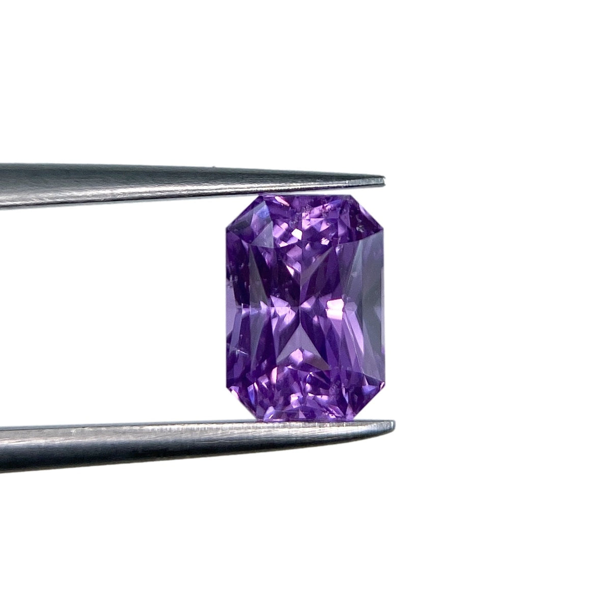 1.77ct radiant cut violet sapphire gemstone held in metal tweezers against a white background.