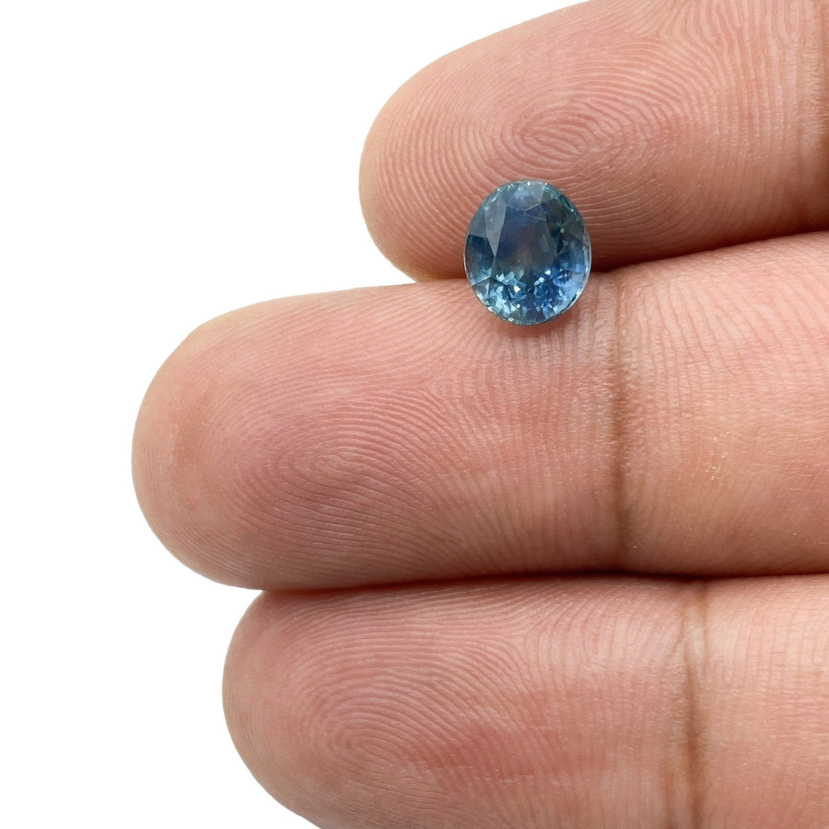 1.96ct oval brilliant cut blue Montana sapphire held between fingers, showcasing its faceted gemstone clarity.