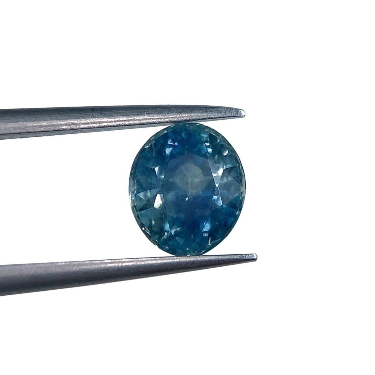 1.96ct oval brilliant cut blue Montana sapphire held in metal tweezers against a white background.