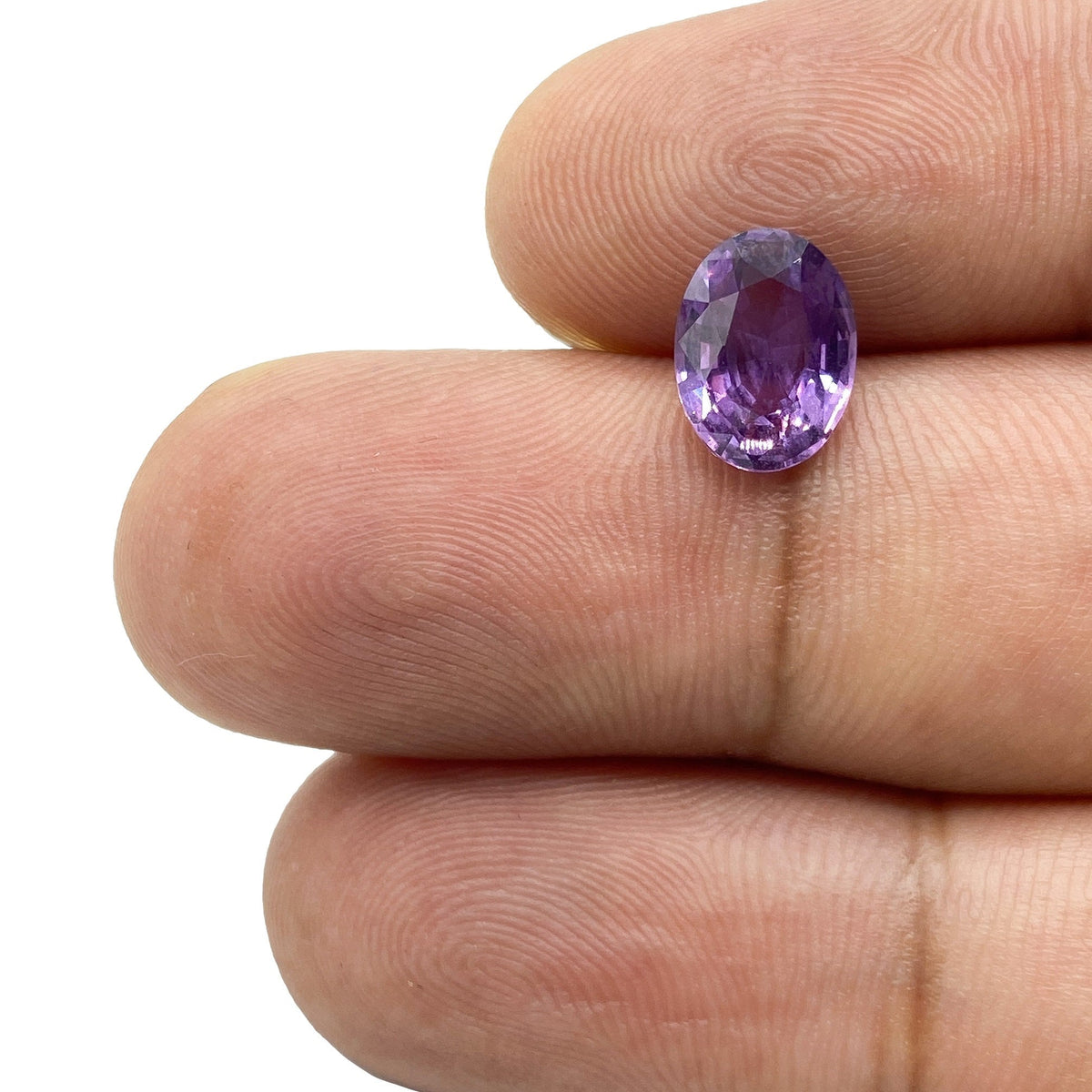 2.02ct brilliant cut oval pinkish purple sapphire gemstone held between fingers.